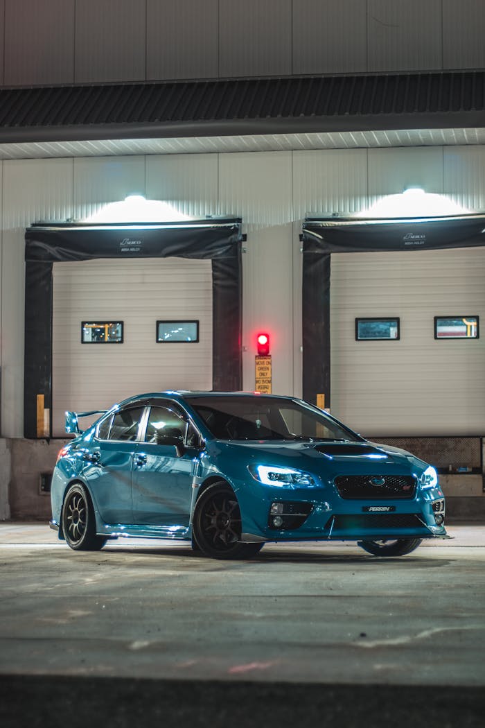 A blue racecar parked outside a closed garage, illuminated under night lights.